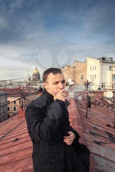 Young Caucasian man smokes cigar on the roof in Saint-Petersburg, Russia