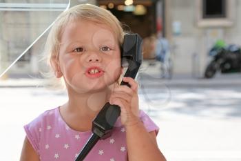 Outdoor portrait of little Caucasian girl talking on the street phone