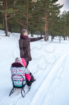 Caucasian family on the winter walking. Mother pulls sled with her two daughters