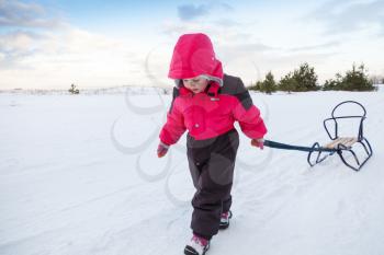 Little baby girl in pink pulling a sled on snowy winter road