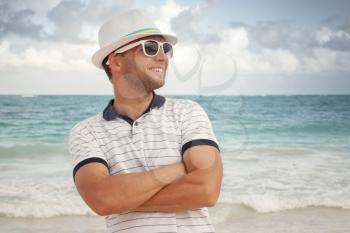 Outdoor portrait of young smiling Caucasian man in white hat and sunglasses on the sea coast