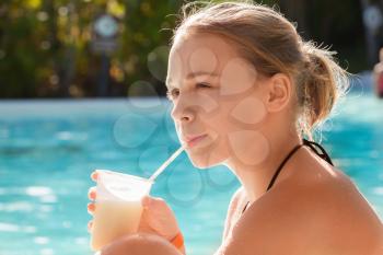 Little blond girl drinks cocktail through plastic tube in swimming pool
