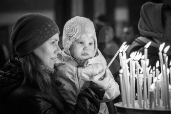 Mother and her little blond Caucasian daughter with candles in Orthodox Russian Church. Black and white photo