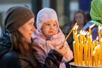 Young mother and her little blond Caucasian daughter with candles in Orthodox Russian Church