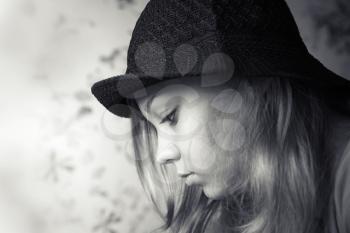 Monochrome closeup profile portrait of beautiful blond teenage girl in black hat