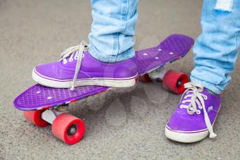 Young skateboarder in gumshoes and jeans stands. Close-up fragment of skateboard and feet