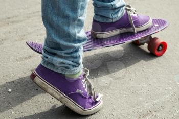 Young skateboarder in jeans standing on his skate. Close-up fragment of skateboard and feet