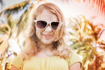 Blond smiling teenager girl in sunglasses, closeup outdoor summer portrait with palms on a background, colorful toned photo with instagram retro style filter effect