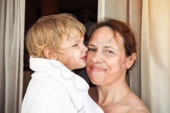 Young happy mother and her cute blond baby girl in white towel after taking a bath, closeup portrait with selective focus