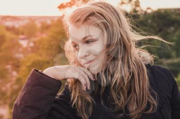 Outdoor closeup portrait of smiling teenage Caucasian blond girl with bright evening sunlight back light