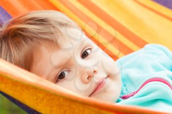 Cute blond baby girl lying in striped hammock, outdoor close-up portrait