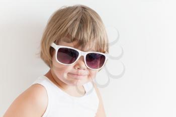 Cute smiling Caucasian little girl in shirt and sunglasses on white wall background, closeup studio portrait