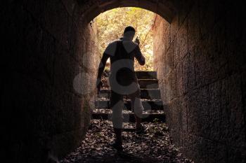 Young man with radio set goes out of dark stone tunnel, warm toned photo, old style filter