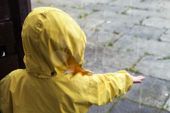 Little child in yellow raincoat playing with rain water drops