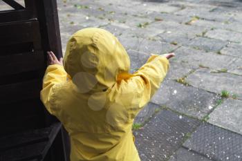 Little child in yellow raincoat playing with water drops