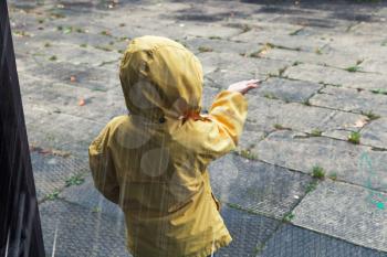 Little child in yellow raincoat playing with raindrops. Vintage tonal correction photo filter effect