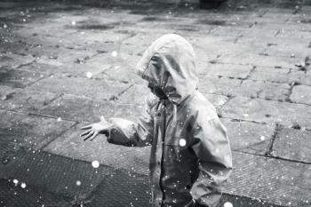 Little child in raincoat playing with raindrops. Monochrome stylized photo