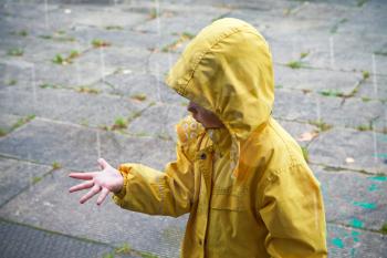 Little child in yellow raincoat playing with raindrops