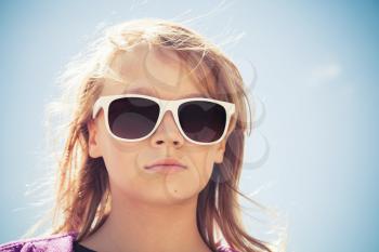 Beautiful blond Caucasian girl in sunglasses, outdoor closeup portrait over blue sky background