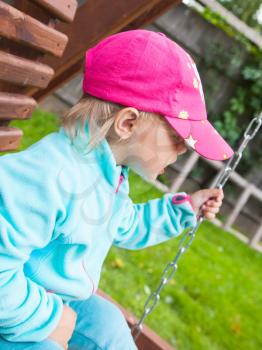 Outdoor portrait of funny little child in a pink baseball cap on a swing