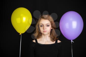 Studio portrait of teenage Caucasian blond girl with yellow and purple balloons over black background