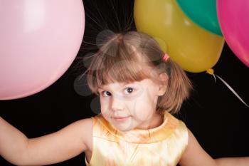 Studio portrait of smiling little Caucasian blond girl with colorful balloons