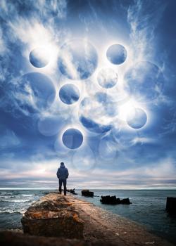 Abstract space fantasy illustration. Man starring at the glowing planet spheres in dramatic blue sky with clouds