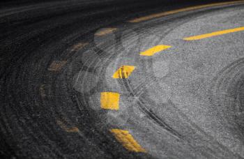 Abstract turning road background with tires track and yellow striped road marking on dark asphalt