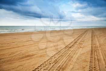 Perspective of tyre tracks on sandy beach with dark blue cloudy sky