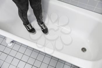 Teenager in black sporty sneakers stands in white bath, feet only