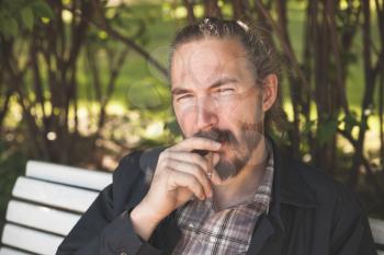 Bearded man smoking cigar in summer park, outdoor portrait with selective focus