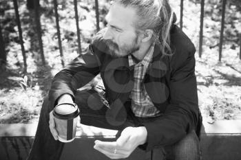 Bearded Asian man with coffee in paper cup, outdoor black and white portrait with selective focus 