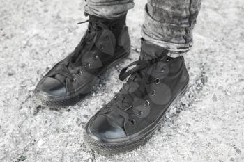 Teenager feet in black gumshoes standing on gray rough concrete floor