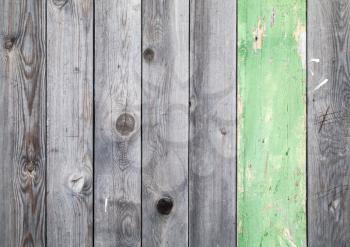 Background texture of old gray weathered wooden lining boards with one green painted plank