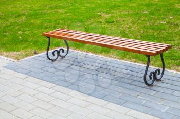 Empty wooden bench stands on cobblestone in summer park near green grass