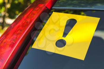 Warning yellow sticker with black exclamation sign over rear window of modern car, novice driver
