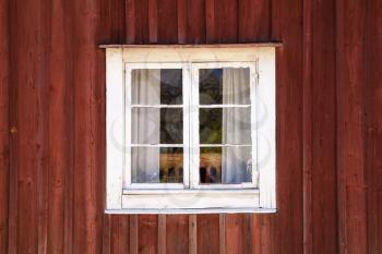 Old dark red wooden wall with window in white frame, typically Scandinavian living house architecture detail