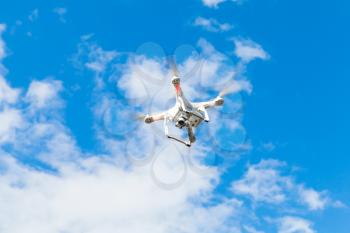 White quadrocopter flying in blue cloudy sky, drone controlled by wireless remote