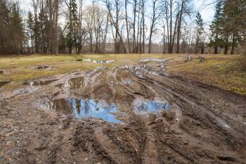 Dirty rural road with puddles and mud, springtime in Russian countryside