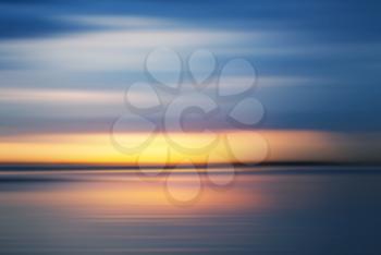Colorful sunset over sea coast under dark blue evening sky. Blurred background photo with motion blur effect