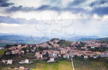 Rural panorama of Italian countryside. Province of Fermo, Italy. Village on a hill under dramatic cloudy sky