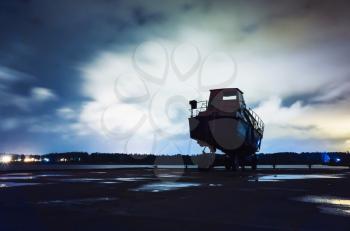 Motor boat sands on transport trailer in port at night, silhouette over cloudy sky