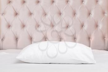 Luxury empty bedroom interior fragment, soft pink headboard, white pillow lays on wide empty bed