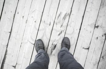 Male feet in leather shoes stand on white wooden pier floor, first person view
