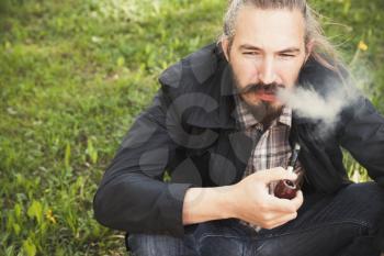 Asian man smoking a pipe on green grass in park, closeup photo with selective focus