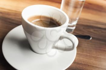 Cup of espresso coffee and small glass of fresh water stand on wooden table