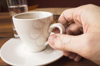 Male hand holds white cup of espresso coffee. Closeup photo with selective focus
