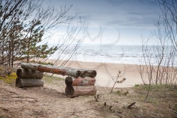 Empty rough wooden bench stands on Baltic Sea coast in spring season. Coastal landscape