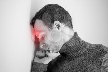 Young adult man with headache near white wall. Black and white stylized photo with red local ache spot