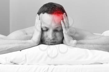Portrait of Young man in bed with headache. Black and white stylized photo with red local ache spot
